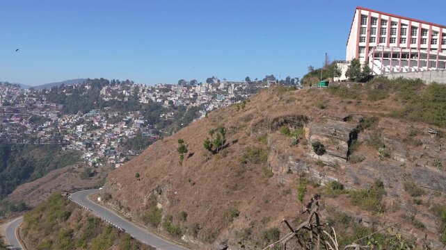 Wide view of Uday Shankar Natya Academy building on cliff top with winding road and Almora city backdrop, Uttarakhand 4K