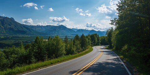 Fototapeta premium A winding mountain road bordered by lush trees under a bright blue sky with clouds, ideal for scenic drives and outdoor activities