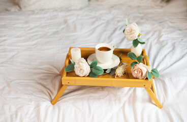 Romantic morning. Wooden coffee table with flowers on bed, white roses. Interior white tones. High quality photo.