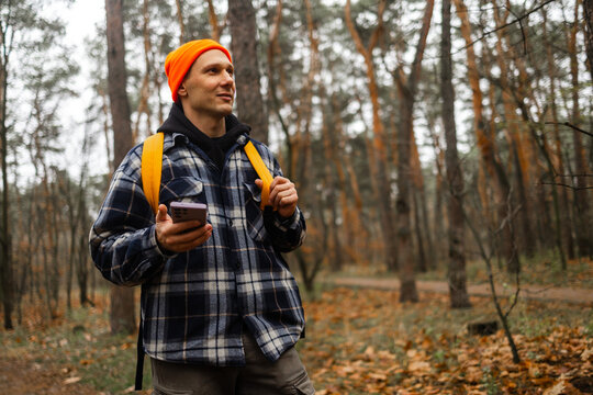 Happy Caucasian hiker with smart phone walking in autumn forest during a rainy day.