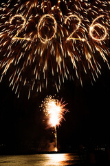 2026 happy new year text of sparklers and colorful fireworks in the night sky over sea surface