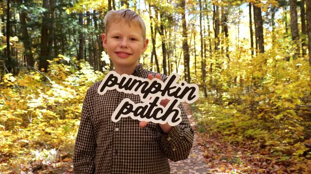 Smiling Boy holds up words Pumpkin Patch in the Forest with Yellow Leaves in the Fall 4K Video Stock Footage