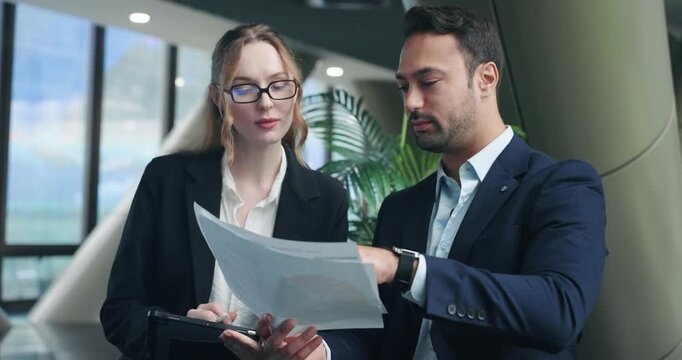 Two happy corporate colleagues laugh joyfully while reviewing business papers and charts together in a modern office building demonstrating successful teamwork and positive work atmosphere - Powered by Adobe