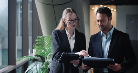 Professional business colleagues discuss and work together on a project while walking in a modern office hallway holding a digital tablet and documents - Powered by Adobe