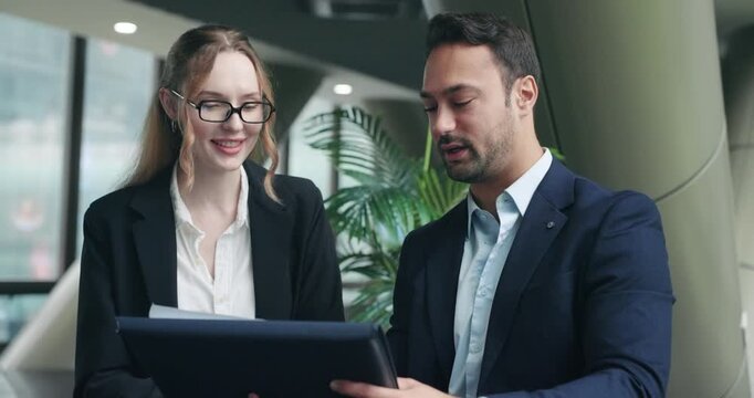 Professional businessman and businesswoman work on a business plan and review statistical papers together while discussing improvements in modern corporate office