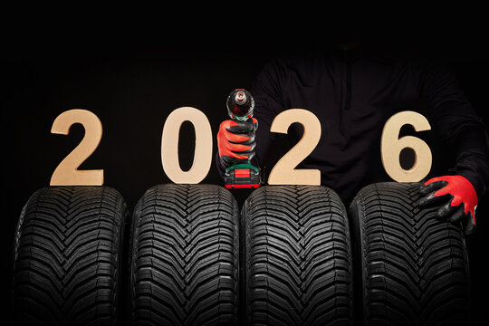 Winter car tires service and hands of mechanic with wheels screwdriver and text 2026 happy new year on black background - Powered by Adobe