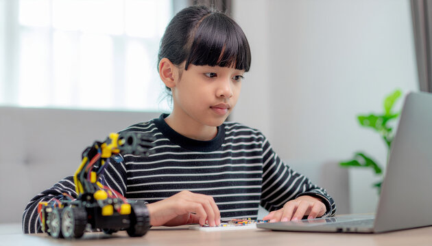 Young girl building electronic robot kit at laptop, focused and thoughtful expression