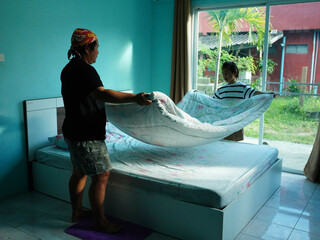 Mother and Daughter Making Bed Together in a Bright Bedroom.