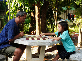 Father and Daughter Playing Checkers (Draughts) Game Outdoors on Stone Table.