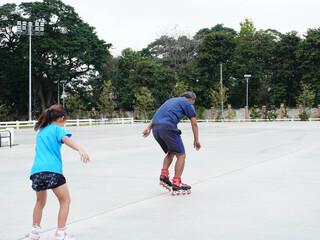 A father and daughter are roller skating together outdoors.