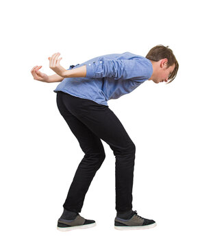 Side view young male student in stooped pose, leaning forward with his back curved and his arms bent behind him as he carries a heavy, invisible load or is in a position of cowering or physical strain