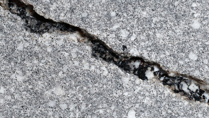 Detailed macro shot of a prominent, dark crack cutting through a textured grey surface, illustrating natural wear, structural imperfection, and raw material erosion