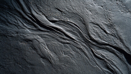 Textured dark grey stone surface with flowing patterns and natural erosion marks, abstract background