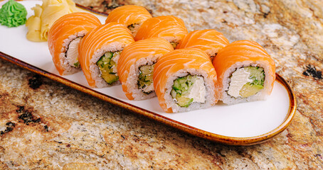 Sushi rolls with fresh salmon on a white plate displayed on a granite table