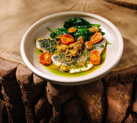 Fresh fish dish with spinach and tomatoes served on a wooden table