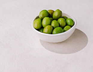 Green olives in a bowl on a light background at a dining table