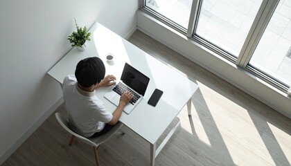 Man Working on Laptop at Minimalist White Desk near Window in Bright Sunlight