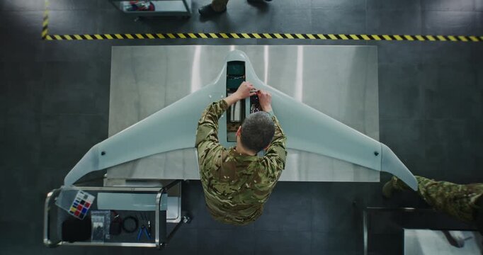 Engineer in Military Uniform Assembling Unmanned Aerial Vehicle. Man in Camouflage, Working on Internal Components of Fixed Wing UAV. Concept Precision of Military Technology Production. Top View.