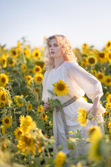 Beautiful blonde girl in a white dress in a field of sunflowers