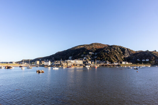 Moored boats on calm water facing Barmouth town illuminated by clear bright morning light