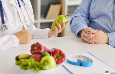 Dietitian and patient discuss nutrition and weightloss. Close view shows a healthcare professional holding a pepper beside tape measure and clipboard. Concept: weight management through diet.
