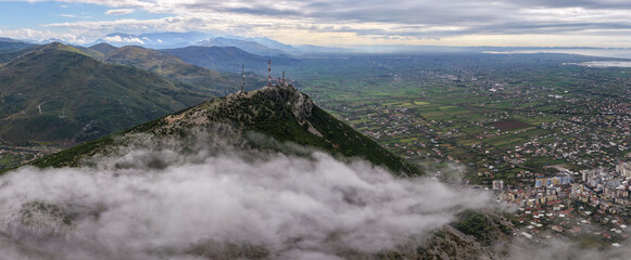 Aerial panorama of Skanderbeg’s Tomb Peak above drifting fog, overlooking the vast Lezhë valley and the distant Adriatic Sea.
