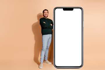 Confident young man in casual attire smiling beside a blank white poster against a beige background promoting creativity