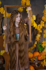 A girl with long hair in a picture frame in a studio surrounded by autumn leaves and pumpkins