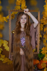 A girl with long hair in a picture frame in a studio surrounded by autumn leaves and pumpkins