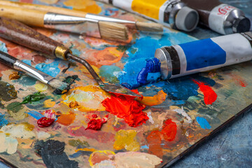 Obraz premium Old used brushes and palette knife in an artist's studio, palette with multi-colored spots of oil or acrylic paint, paint tubes