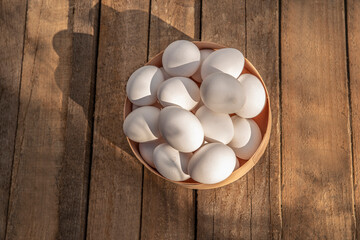 Chicken eggs in wooden bowl on grunge table in chicken coop, barn. Countryside outdoor setting in the backyard © TSViPhoto