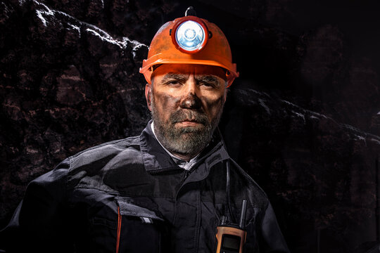 Coal miner with a dirty face in black dust, wearing a protective helmet with a flashlight and work clothes for working in a mine. Hard work underground in a coal mine, digging site.