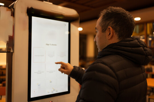 Man using touchscreen self-service kiosk ordering food or drinks