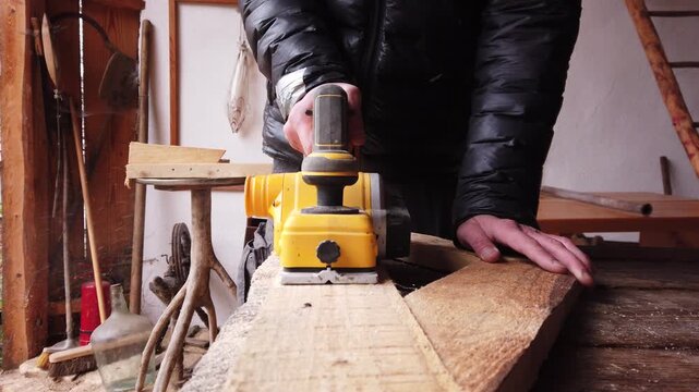 Hands of carpenter working with cordless brushless planer smoothing wooden board