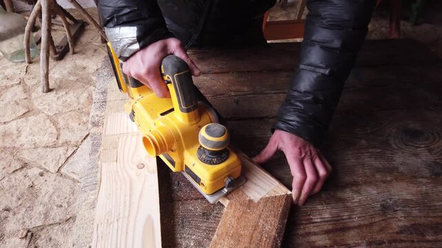 Hands of carpenter working with cordless brushless planer smoothing wooden board