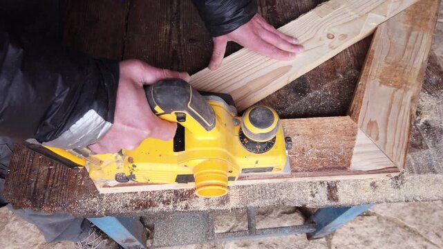 Hands of carpenter working with cordless brushless planer smoothing wooden board
