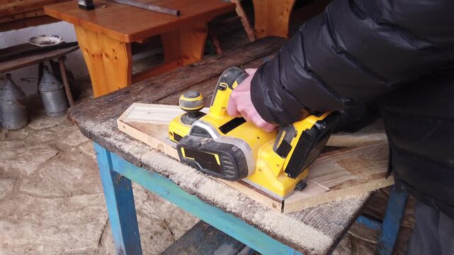 Hands of carpenter working with cordless brushless planer smoothing wooden board
