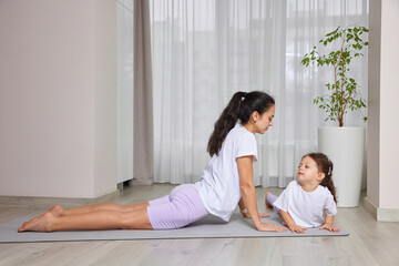 Mother and daughter practicing cobra pose on yoga mat, enjoying fitness and healthy lifestyle