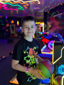 Young boy holding basketball in vibrant neon arcade