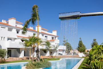 Outdoor shower by swimming pool at modern white villa with tropical landscaping and blue sky