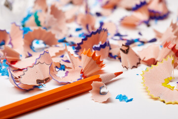 Orange pencil tip surrounded by colorful wood shavings on a white background