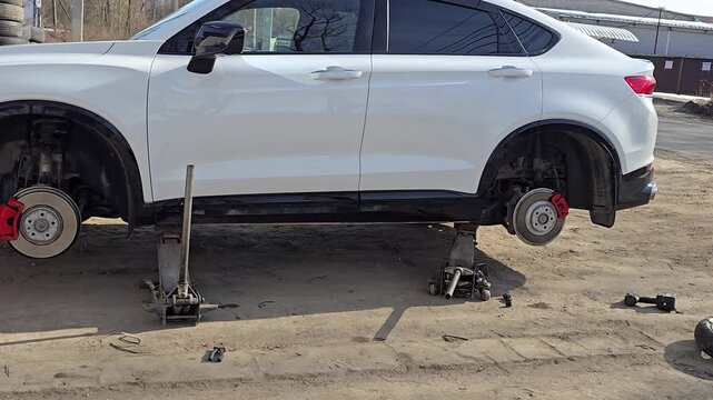 Moscow, December 01 2025, white car with a flat tire is being lifted up by a jack. The tire is missing and the car is on a dirt road
