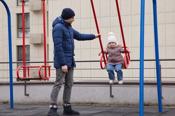 Father and daughter enjoying time together on a playground swing during winter