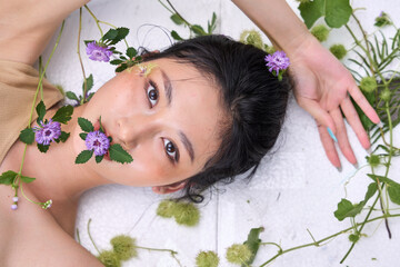 lose-up of a young woman's face partially submerged or surrounded by water and floating flowers.