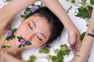 Young woman lying on her back with arms extended, amid a backdrop of vines and foliage."