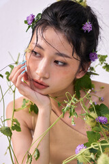 Young woman with a floral crown, looking downward in a thoughtful pose amid greenery."