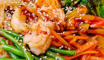 Colorful shrimp stir-fry with vegetables and sesame seeds served on noodles