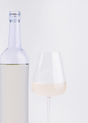Glass of white wine beside a clear bottle on a neutral background
