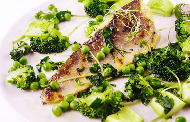 Freshly cooked fish with broccoli, peas, and herbs on a white plate