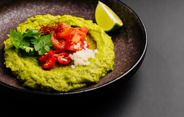 Delicious green avocado dip served with fresh toppings and lime wedge